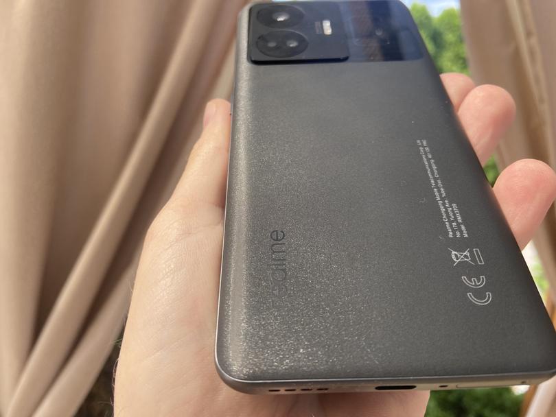 Smartfon realme GT3 w kolorze czarnym na tle ogrodu.